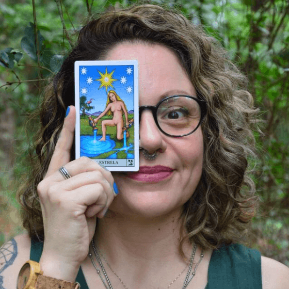 Luana segurando a carta A Estrela do tarot, em meio à natureza